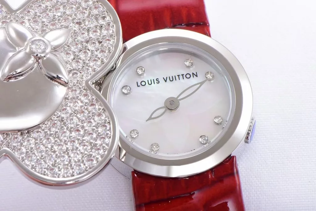 Louis Vuitton Women's Watch Vivienne Bijou Secret, Vivienne Mascot Collection Movement: Quartz. Functions: hour and minute display. Case: 18-carat white gold, 18-carat pink gold, 18-carat yellow gold with diamonds. Diameter: 34 mm. Anti-reflective sapphire crystal. Water-resistant to 30 m. For the first time, LOUIS VUITTON has incorporated its mascot, Vivienne, into the world of watchmaking, with the brave and charming Vivienne doll, dressed in diamond-embellished gold, to create a unique ladies' watch: the Vivienne Bijou Secret. Vivienne's face is movable, covering or revealing the 21 mm white gold case between rotations. The dial, appliquéd with white mother-of-pearl, is adorned with a graceful signature Monogram motif and set with diamond hour markers. The watch is currently available on four straps in red, black, green and white leather.