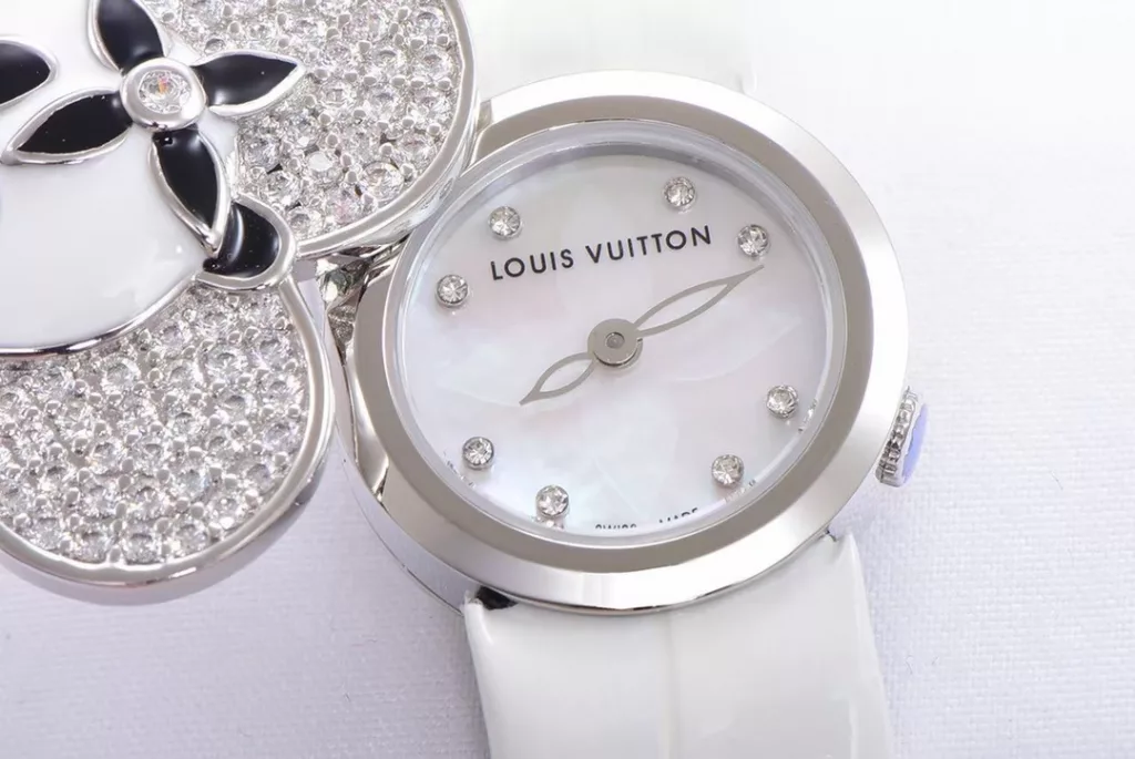 LOUIS VUITTON VIVIENNE BIJOU SECRET Mascot Movement: Quartz Movement Functions: Hours and minutes Case: 18K white gold, 18K pink gold, 18K yellow gold with diamonds Case diameter: 34 mm Anti-reflective sapphire Water-resistant to 30 metres This year, for the first time, LOUIS VUITTON is bringing its mascot, Vivienne, into the world of watchmaking with the Vivienne Bijou Secret. This year, for the first time, LOUIS VUITTON has incorporated the Vivienne doll into the world of watchmaking, with the brave and charming Vivienne doll in a gold dress embellished with diamonds, to create a unique ladies' watch: the Vivienne Bijou Secret. Vivienne's face is movable and will cover or reveal the 21 mm white gold case between rotations. The white mother-of-pearl appliquéd dial is decorated with the graceful signature Monogram motif and set with diamond hour markers. The watch is currently available on four straps in red, black, green and white leather.