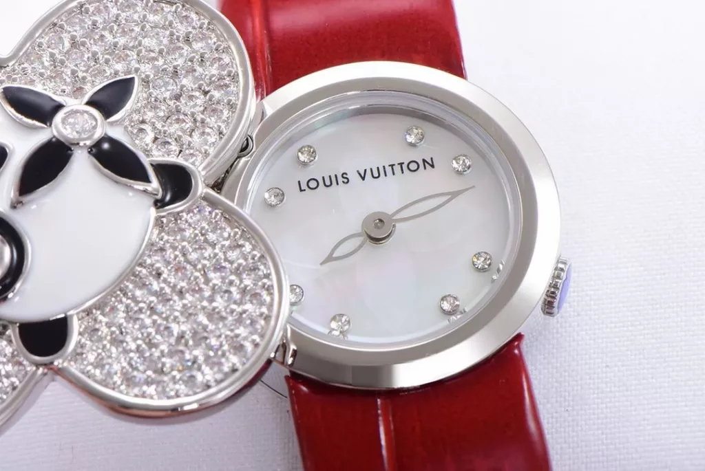 LOUIS VUITTON VIVIENNE BIJOU SECRET Mascot Movement: Quartz Movement Functions: Hours and minutes Case: 18K white gold, 18K pink gold, 18K yellow gold with diamonds Case diameter: 34 mm Anti-reflective sapphire Water-resistant to 30 metres This year, for the first time, LOUIS VUITTON is bringing its mascot, Vivienne, into the world of watchmaking with the Vivienne Bijou Secret. This year, for the first time, LOUIS VUITTON has incorporated the Vivienne doll into the world of watchmaking, with the brave and charming Vivienne doll in a gold dress embellished with diamonds, to create a unique ladies' watch: the Vivienne Bijou Secret. Vivienne's face is movable and will cover or reveal the 21 mm white gold case between rotations. The white mother-of-pearl appliquéd dial is decorated with the graceful signature Monogram motif and set with diamond hour markers. The watch is currently available on four straps in red, black, green and white leather.