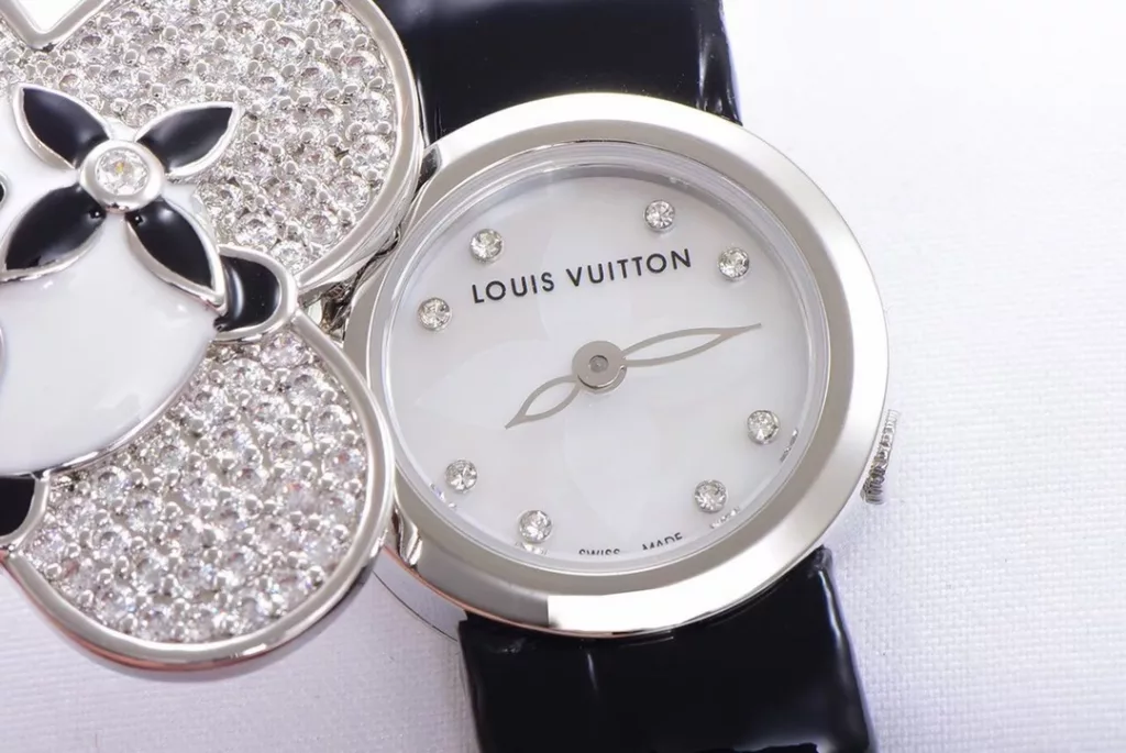 LOUIS VUITTON VIVIENNE BIJOU SECRET Mascot Movement: Quartz Movement Functions: Hours and minutes Case: 18K white gold, 18K pink gold, 18K yellow gold with diamonds Case diameter: 34 mm Anti-reflective sapphire Water-resistant to 30 metres This year, for the first time, LOUIS VUITTON is bringing its mascot, Vivienne, into the world of watchmaking with the Vivienne Bijou Secret. This year, for the first time, LOUIS VUITTON has incorporated the Vivienne doll into the world of watchmaking, with the brave and charming Vivienne doll in a gold dress embellished with diamonds, to create a unique ladies' watch: the Vivienne Bijou Secret. Vivienne's face is movable and will cover or reveal the 21 mm white gold case between rotations. The white mother-of-pearl appliquéd dial is decorated with the graceful signature Monogram motif and set with diamond hour markers. The watch is currently available on four straps in red, black, green and white leather.