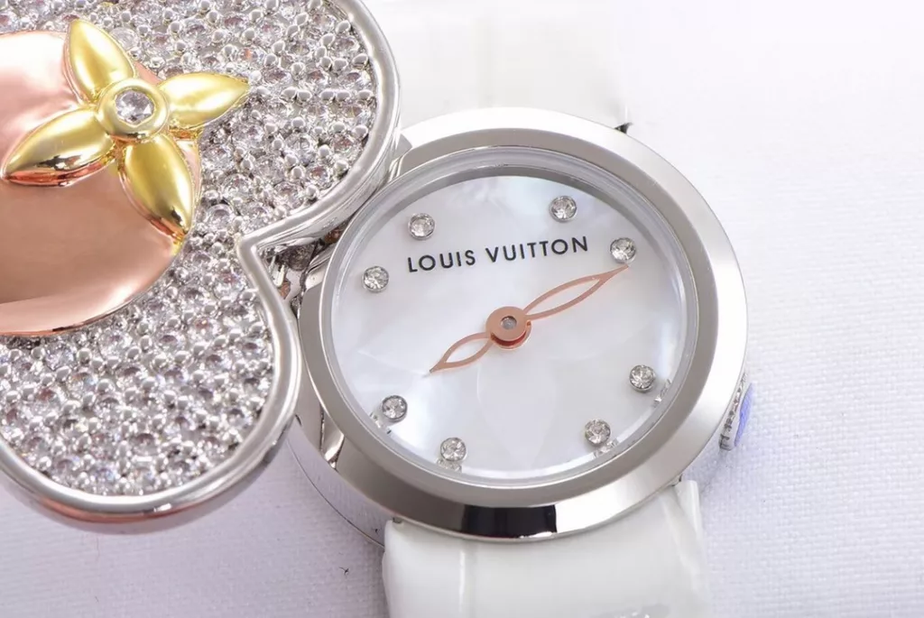 LOUIS VUITTON VIVIENNE BIJOU SECRET Mascot Movement: Quartz Movement Functions: Hours and minutes Case: 18K white gold, 18K pink gold, 18K yellow gold with diamonds Case diameter: 34 mm Anti-reflective sapphire Water-resistant to 30 metres This year, for the first time, LOUIS VUITTON is bringing its mascot, Vivienne, into the world of watchmaking with the Vivienne Bijou Secret. This year, for the first time, LOUIS VUITTON has incorporated the Vivienne doll into the world of watchmaking, with the brave and charming Vivienne doll in a gold dress embellished with diamonds, to create a unique ladies' watch: the Vivienne Bijou Secret. Vivienne's face is movable and will cover or reveal the 21 mm white gold case between rotations. The white mother-of-pearl appliquéd dial is decorated with the graceful signature Monogram motif and set with diamond hour markers. The watch is currently available on four straps in red, black, green and white leather.