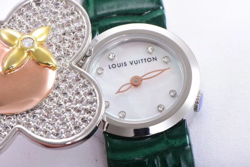 LOUIS VUITTON VIVIENNE BIJOU SECRET Mascot Movement: Quartz Movement Functions: Hours and minutes Case: 18K white gold, 18K pink gold, 18K yellow gold with diamonds Case diameter: 34 mm Anti-reflective sapphire Water-resistant to 30 metres This year, for the first time, LOUIS VUITTON is bringing its mascot, Vivienne, into the world of watchmaking with the Vivienne Bijou Secret. This year, for the first time, LOUIS VUITTON has incorporated the Vivienne doll into the world of watchmaking, with the brave and charming Vivienne doll in a gold dress embellished with diamonds, to create a unique ladies' watch: the Vivienne Bijou Secret. Vivienne's face is movable and will cover or reveal the 21 mm white gold case between rotations. The white mother-of-pearl appliquéd dial is adorned with a graceful signature Monogram motif and set with diamond hour markers. The watch is currently available on four straps in red, black, green and white leather.